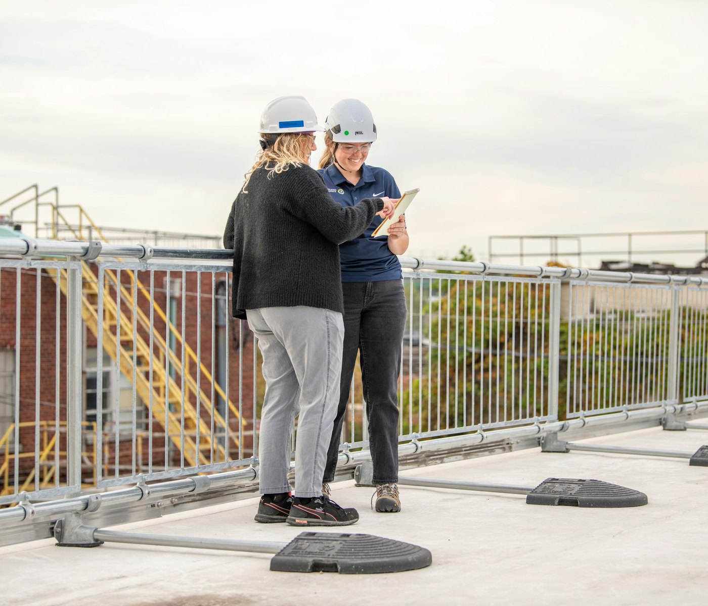 Two people in hard hats reviewing a project on a tablet on a rooftop jobsite