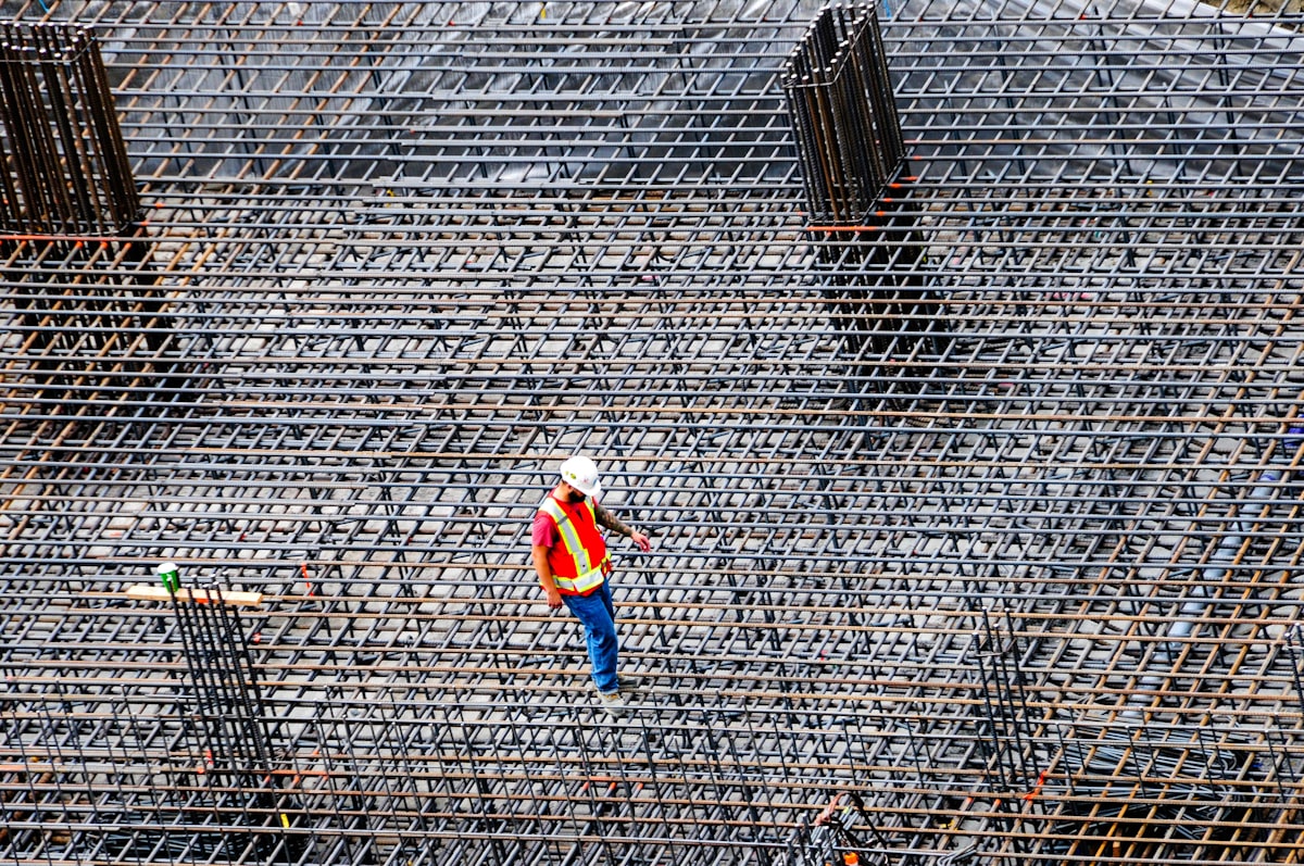 A field superintendent in a hard hat and hi-vis vest on the rebar deck of an active commercial construction site