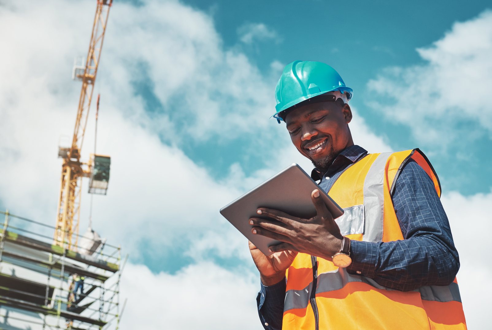 A contractor checking a tablet on site beneath a tower crane